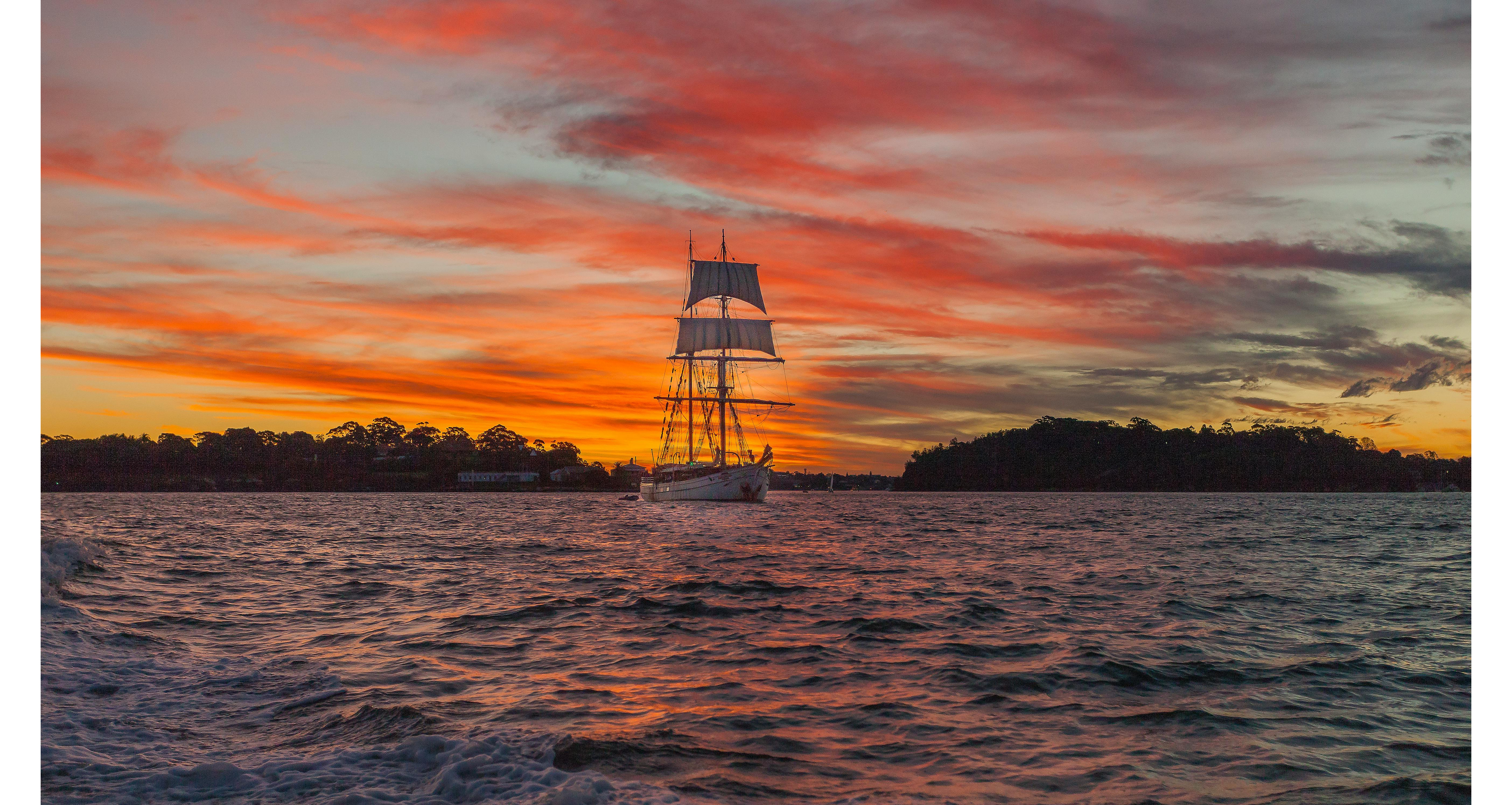 Tall-masted sailing ship in front of a sunset