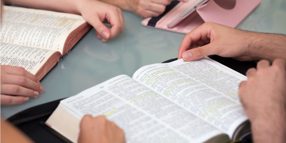 Closeup of multiple people with open Bibles at a table